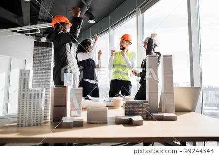 Successful team of coworkers builders and architects are raising hands in fists and screaming Successful team of coworkers builders and architects are raising hands in fists and screaming 99244343