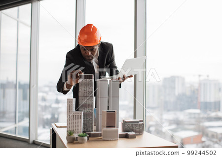Confident afro-american man in suit using laptop looking at the architecture design of buildings 99244502