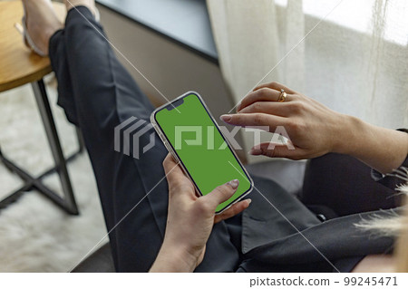 a woman's hand holds a modern smartphone on a green street background.close up.green screen for your design.copy-space 99245471