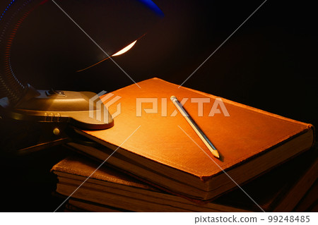 The included lamp and a stack of old books on the desk. Education concept. The included lamp and a stack of old books on the desk. Education concept. 99248485