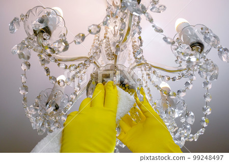 Close-up of gloved hands wipes dust from the chandelier. House cleaning Close-up of gloved hands wipes dust from the chandelier. House cleaning 99248497