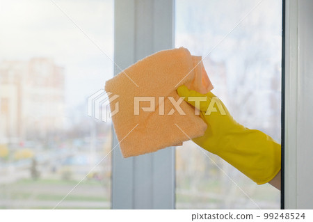 A female hand in a yellow glove wipes a dirty window. House cleaning. Household concept. A female hand in a yellow glove wipes a dirty window. House cleaning. Household concept. 99248524