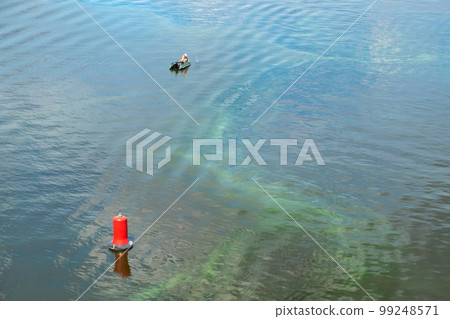 A man in a rubber boat is fishing on a dirty river. Ecological problems, environmental pollution 99248571