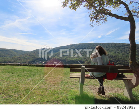 A woman relaxing on a bench with a magnificent view in the background 99248982