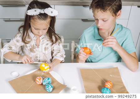 Portrait two children, little girl, boy siblings, painting multi coloring Easter eggs in kitchen, paintbrush. Top view Portrait two children, little girl, boy siblings, painting multi coloring Easter eggs in kitchen, paintbrush. Top view 99249275