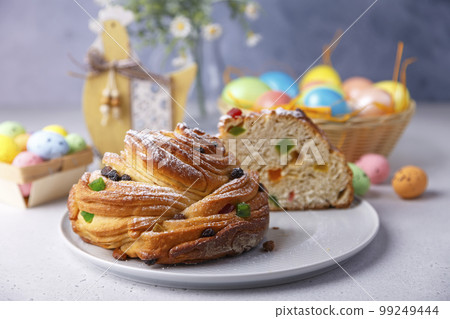 Craffin (Cruffin) with raisins and candied fruits sprinkled with powdered sugar. Traditional Easter Bread Kulich and painted eggs on a gray background. Easter Holiday. Close-up, selective focus. Craffin (Cruffin) with raisins and candied fruits sprinkled with powdered sugar. Traditional Easter Bread Kulich and painted eggs on a gray background. Easter Holiday. Close-up, selective focus. 99249444