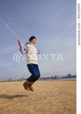 Elementary school girl jumping rope in a park on the coast in winter 99250009