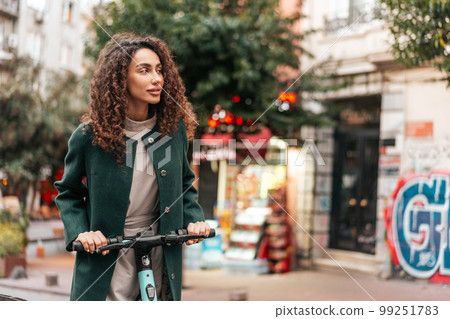 Young curly woman with electric scooter at the city Young curly woman with electric scooter at the city 99251783