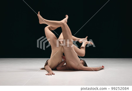 Legs up. Two young girls, contemp dancers in bodysuits performing in experimental style over black background. Creativity and inspiration Legs up. Two young girls, contemp dancers in bodysuits performing in experimental style over black background. Creativity and inspiration 99252084