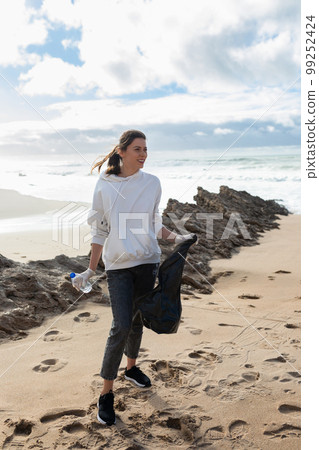 Earth day. Young female activist putting plastic bottles in a garbage bag, cleaning coastal zone, cropped, vertical shot 99252424