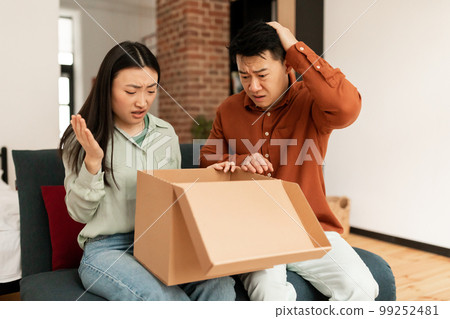 Upset asian spouses looking at cardboard box, having problems with delivery of goods at home, copy space 99252481
