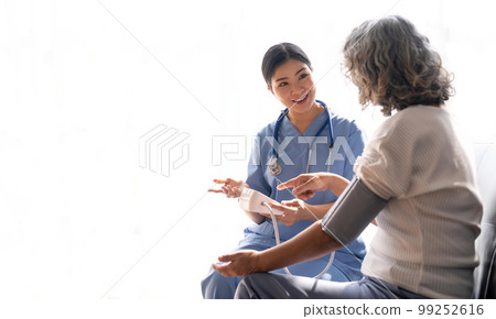 Happy senior woman having her blood pressure measured in a nursing home by her caregiver. Happy nurse measuring blood pressure of a senior woman 99252616