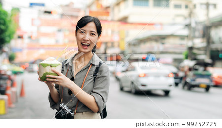 Happy young Asian woman backpack traveler drinking a coconut juice at China town street food market in Bangkok, Thailand. Traveler checking out side streets. 99252725