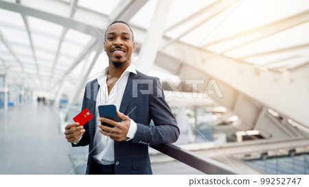 Portrait Of Smiling Black Man With Smartphone And Credit Card At Airport Portrait Of Smiling Black Man With Smartphone And Credit Card At Airport 99252747