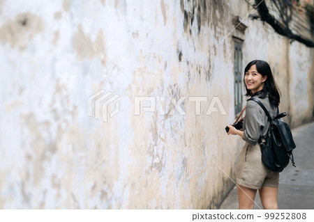 Young Asian woman backpack traveler using digital compact camera, enjoying street cultural local place and smile. Traveler checking out side streets. Young Asian woman backpack traveler using digital compact camera, enjoying street cultural local place and smile. Traveler checking out side streets. 99252808