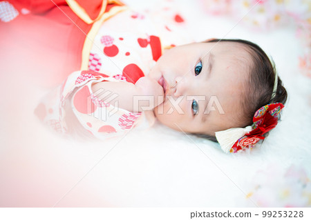 A cute girl baby in a red hakama surrounded by spring cherry blossoms 99253228
