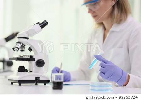 A woman in front microscope and blue reagent in test tube A woman in front microscope and blue reagent in test tube 99253724
