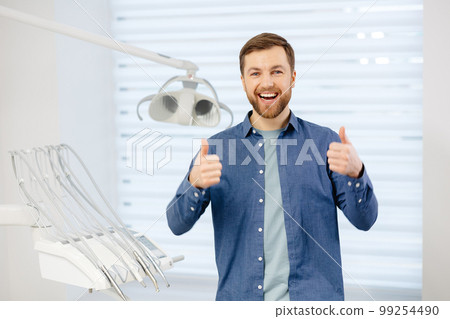 Portrait of happy patient near dental chair and shows a gesture with a thumb up class, good. Modern dentistry with the use of new technologies 99254490