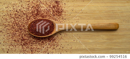Organic aromatic sumac texture in wooden spoon on bamboo cutting board Organic aromatic sumac texture in wooden spoon on bamboo cutting board 99254516