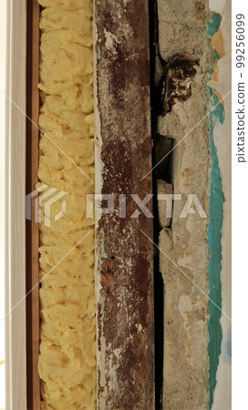 a fragment of the wall next to the doorway with a visible layer structure of the board, mounting foam, plaster and door frame panel in the vertical orientation of the frame close-up a fragment of the wall next to the doorway with a visible layer structure of the board, mounting foam, plaster and door frame panel in the vertical orientation of the frame close-up 99256099