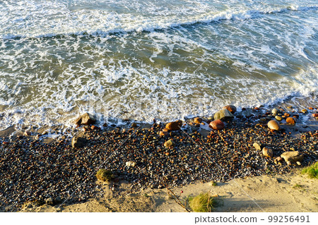 Beautiful view of rocky Baltic Sea coast, sand dune and waves with white foam tops in sunset light 99256491