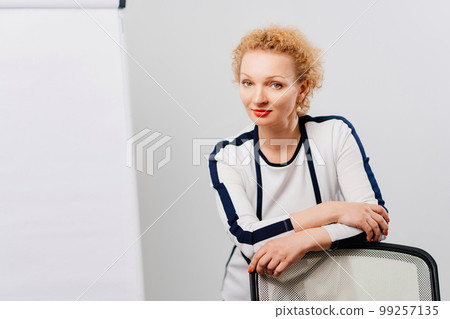 a blonde in a white black suit in an office with a board for meetings. a blonde in a white black suit in an office with a board for meetings. 99257135