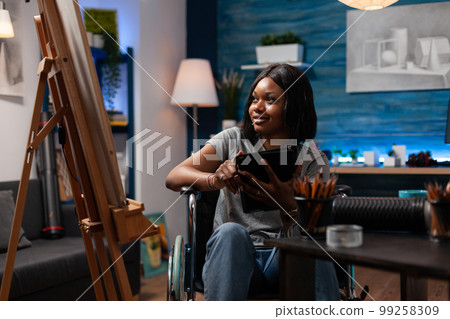 Professional female artist looking for inspiration on internet to create pencil drawing on blank canvas in art studio. African american woman with artistic talent reviewing art notes on tablet. Professional female artist looking for inspiration on internet to create pencil drawing on blank canvas in art studio. African american woman with artistic talent reviewing art notes on tablet. 99258309
