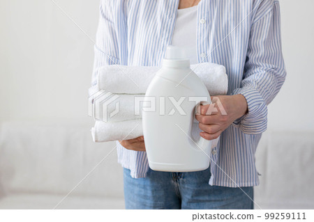 Woman holds stack of white towels bottle of detergent in her hands, of cleaning washing cleanliness Woman holds stack of white towels bottle of detergent in her hands, of cleaning washing cleanliness 99259111