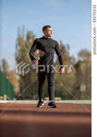 Athletic man walking through the stadium with victory cup 99259332