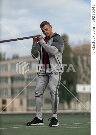 Athletic man in sportswear pumps his biceps with an elastic band Athletic man in sportswear pumps his biceps with an elastic band 99259345