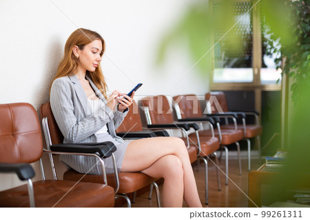 Businesswoman with smartphone sitting in hall 99261311