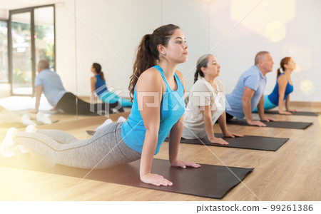 People of different ages performing cobra exercise during group Pilates workout. Active lifestyle and wellness concept People of different ages performing cobra exercise during group Pilates workout. Active lifestyle and wellness concept 99261386