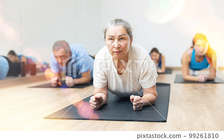 People of different ages in sportswear performing plank exercise during group Pilates workout in fitness studio People of different ages in sportswear performing plank exercise during group Pilates workout in fitness studio 99261810