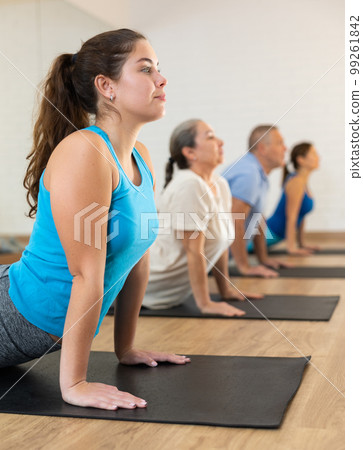 Class of male and women of different ages in active wear doing cobra exercise exercise during Pilates training together in gym Class of male and women of different ages in active wear doing cobra exercise exercise during Pilates training together in gym 99261842