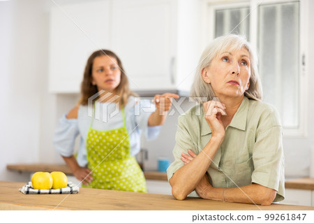 Quarrel of an elderly mother and adult daughter in the kitchen. Adult daughter is unhappy with elderly mother Quarrel of an elderly mother and adult daughter in the kitchen. Adult daughter is unhappy with elderly mother 99261847