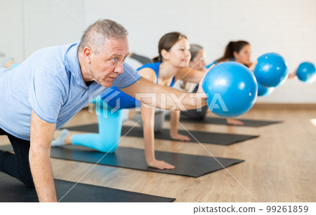 Aged man exercising with pilates ball during group training Aged man exercising with pilates ball during group training 99261859