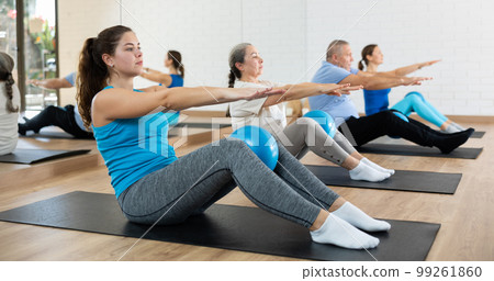 People of different ages pressing core and clutching mini Pilates balls between legs during Pilates training together People of different ages pressing core and clutching mini Pilates balls between legs during Pilates training together 99261860