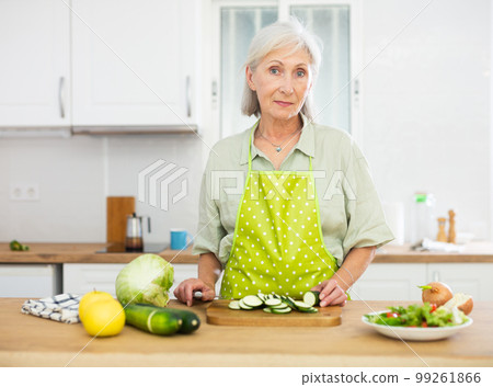 Smiling old woman sclicing vegetables, cooking salad at home 99261866