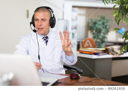 Male doctor in headphones with microphone consults patient on Internet 99261938
