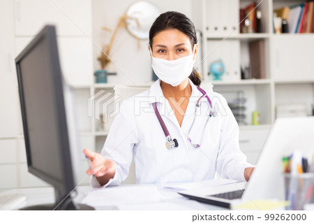 Female doctor in in protective medical mask working on laptop Female doctor in in protective medical mask working on laptop 99262000