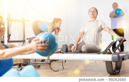 Aged woman practicing pilates on reformer tower equipment in sports hall 99262080