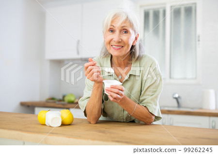 Mature woman eating tasty yogurt in kitchen Mature woman eating tasty yogurt in kitchen 99262245