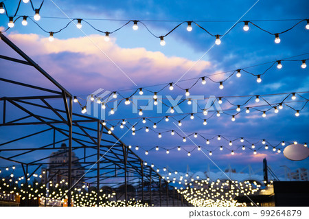 String of light bulb decorations and awning structures for outdoor activities, party, concert, festival, fun fair. Street outside lighted light bulbs garland on night cloudy sky. String of light bulb decorations and awning structures for outdoor activities, party, concert, festival, fun fair. Street outside lighted light bulbs garland on night cloudy sky. 99264879