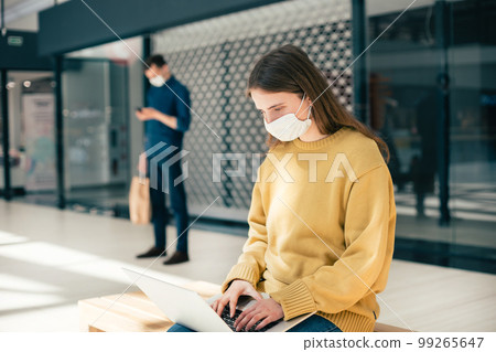 female blogger in a protective mask works on a laptop 99265647