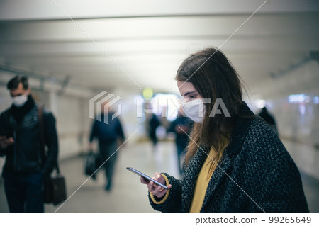 young woman in a protective mask reading a text message at a metro station. young woman in a protective mask reading a text message at a metro station. 99265649
