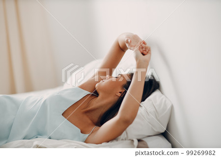 Healthy young woman dressing nightie stretches lying on bed in bedroom. 99269982