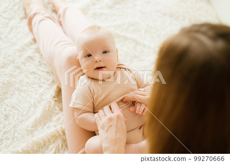 Newborn boy lies on his mother's lap and looks, the mother holds his hands. The concept of happy motherhood 99270666