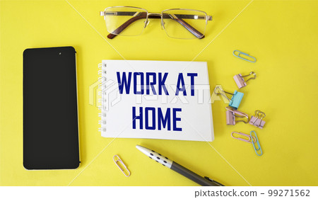 Message about work at home on a notebook, next to a mobile phone, a pen, glasses and paper clips  99271562