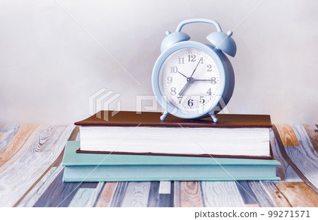 On a light striped background, there are two diaries and a blue alarm clock. On a light striped background, there are two diaries and a blue alarm clock. 99271571
