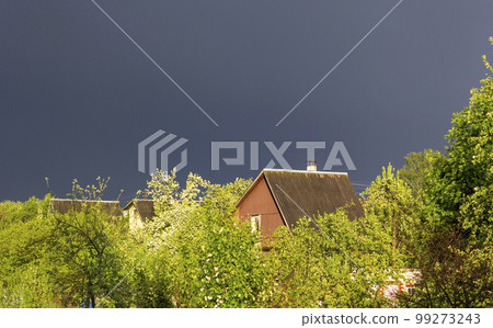 Stormy sky over a small village. The green foliage is illuminated by the sun. Stormy sky over a small village. The green foliage is illuminated by the sun. 99273243